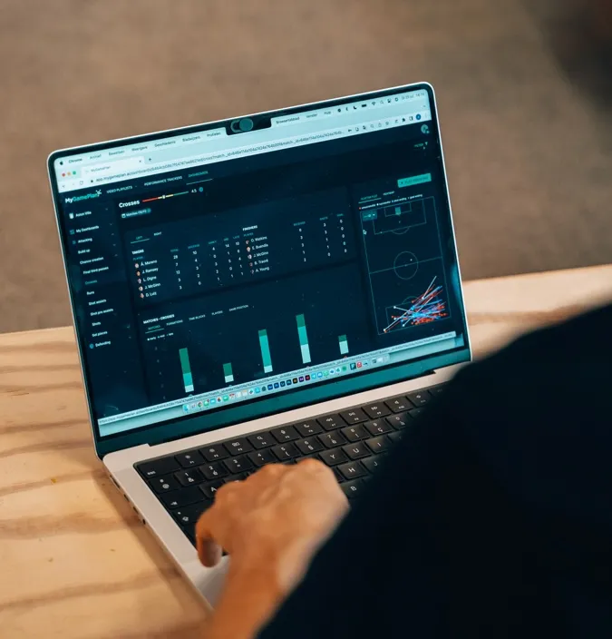 Person using a laptop displaying a sports analytics dashboard with player stats, charts, and a soccer field graphic.
